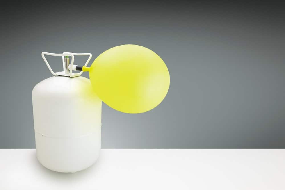 Yellow balloon being filled up by a tank of helium gas.