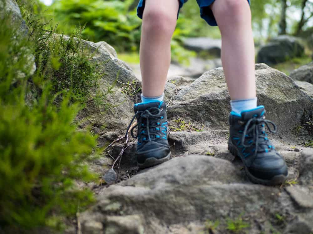 Boy in hiking boots standing over a boulder.