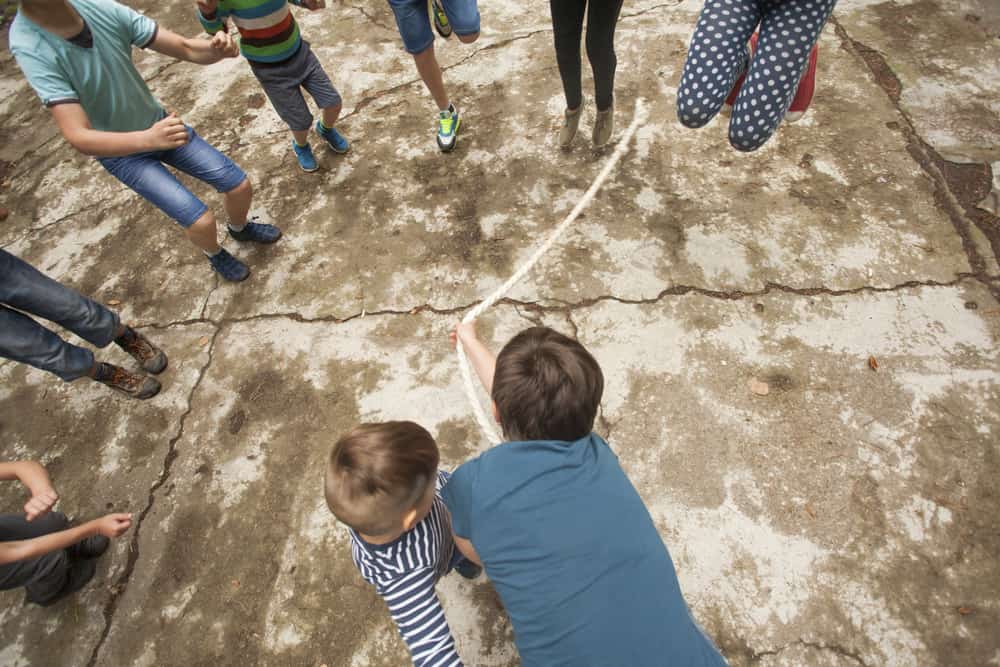 Kids playing jumping rope on the ground.