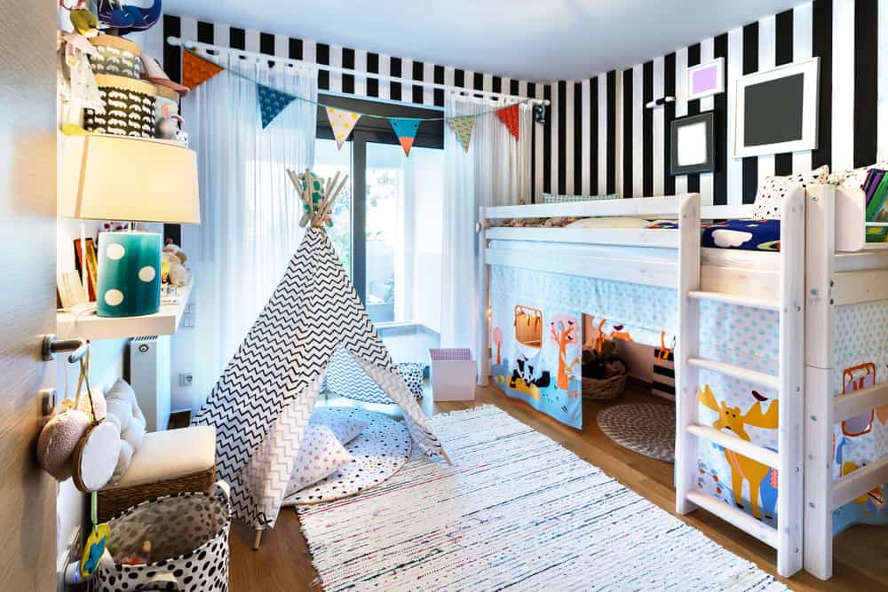 Kid's bedroom with striped walls, a loft bed, a teepee, and a large rug.