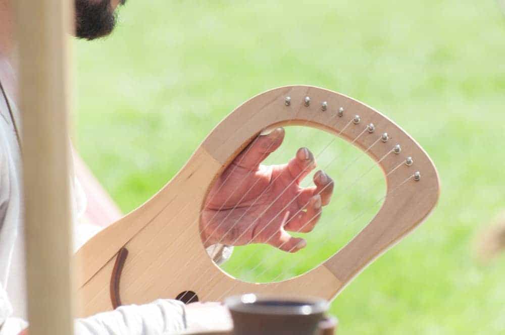 A man playing a medieval harp outdoors.