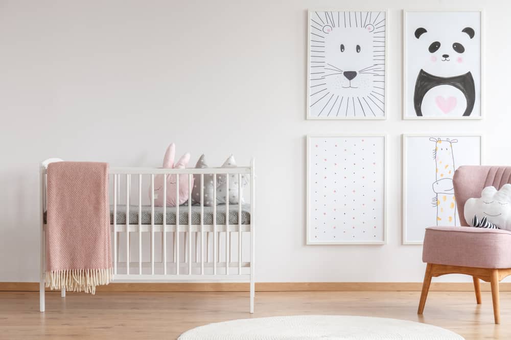 Nursery room with a mini crib, pink upholstered chair, and a cute gallery wall.