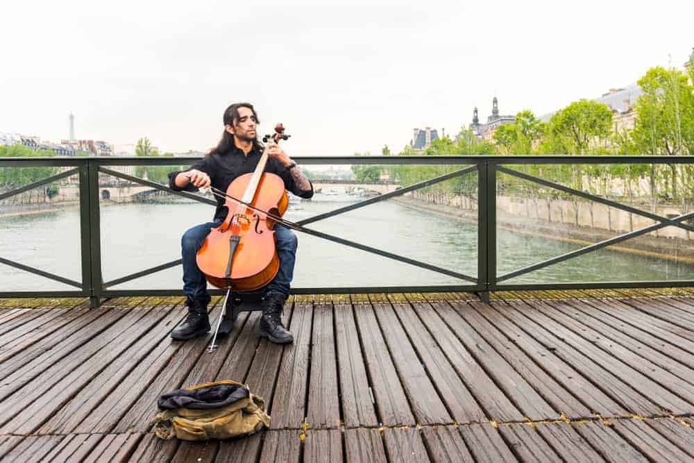 A plays a cello on a scenic wooden bridge.