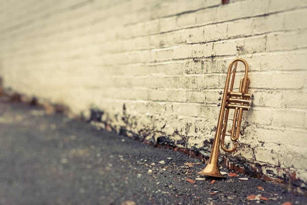 9 Popular Types of Trumpets Explained 13 Old trumpet leaning against distressed-looking dirty white brick wall.