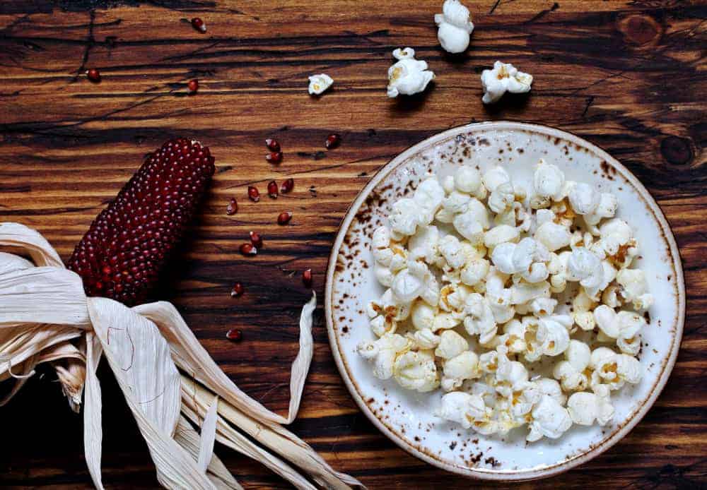 Red corn beside a plate of popcorn.