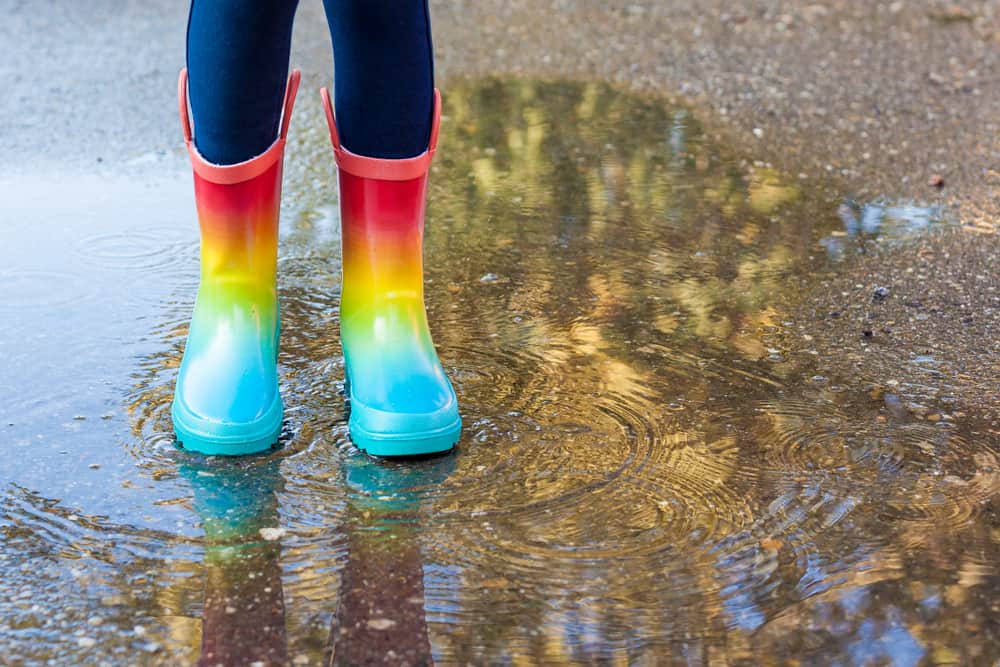Girl wearing colorful rubber boots standing over a puddle.