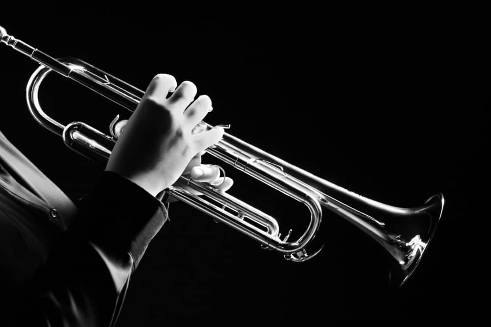 9 Popular Types of Trumpets Explained 11 Musician using a trumpet on black background.