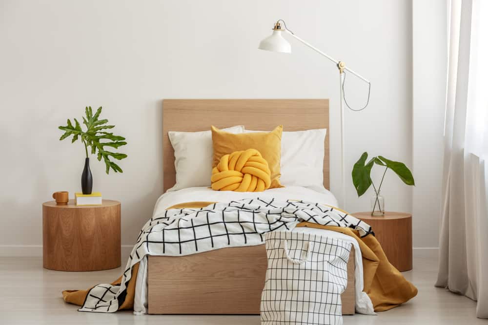 Single bed with a yellow knot pillow, and a plaid blanket matching with the hamper.