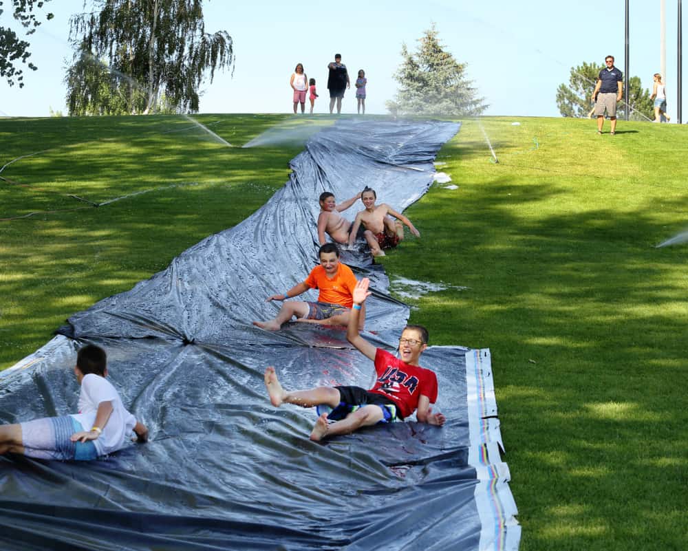 Teens playing slide in the backyard with sprinklers.