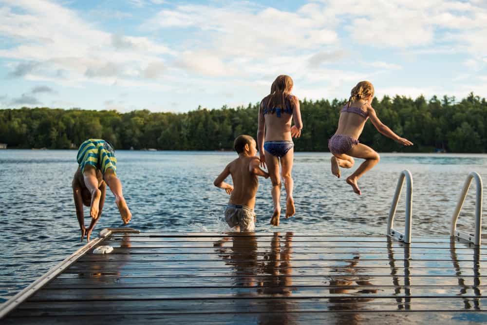 Kids in swimwear jumping into the lake.