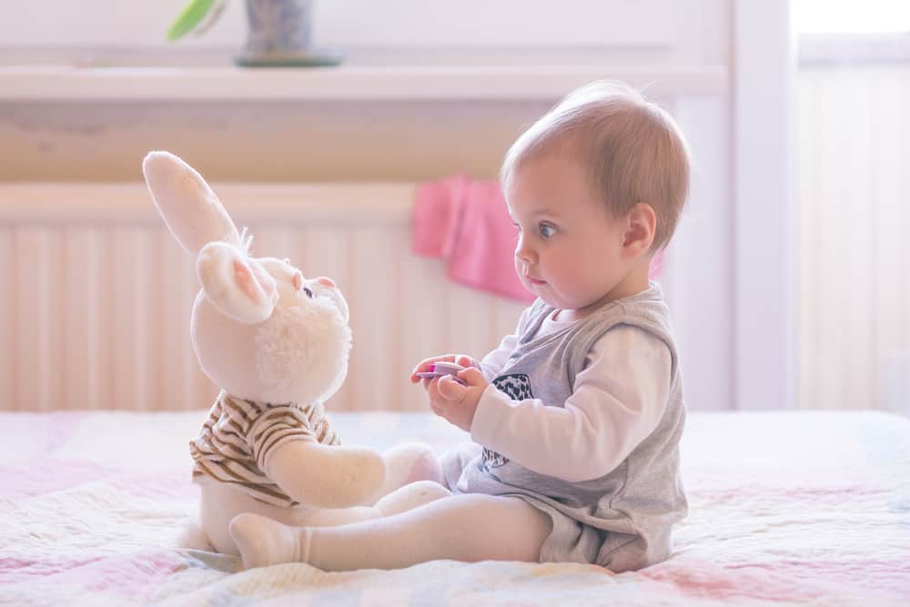 This is a baby girl playing with a stuffed rabbit plush toy.