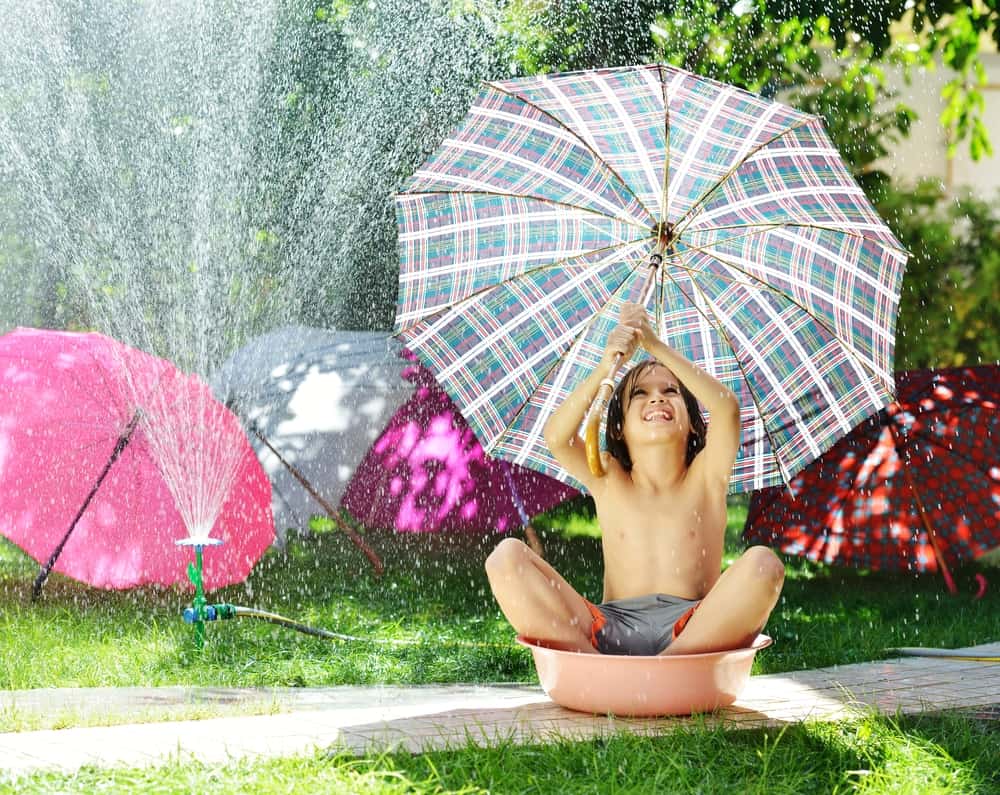A kid playing with umbrellas and sprinklers.