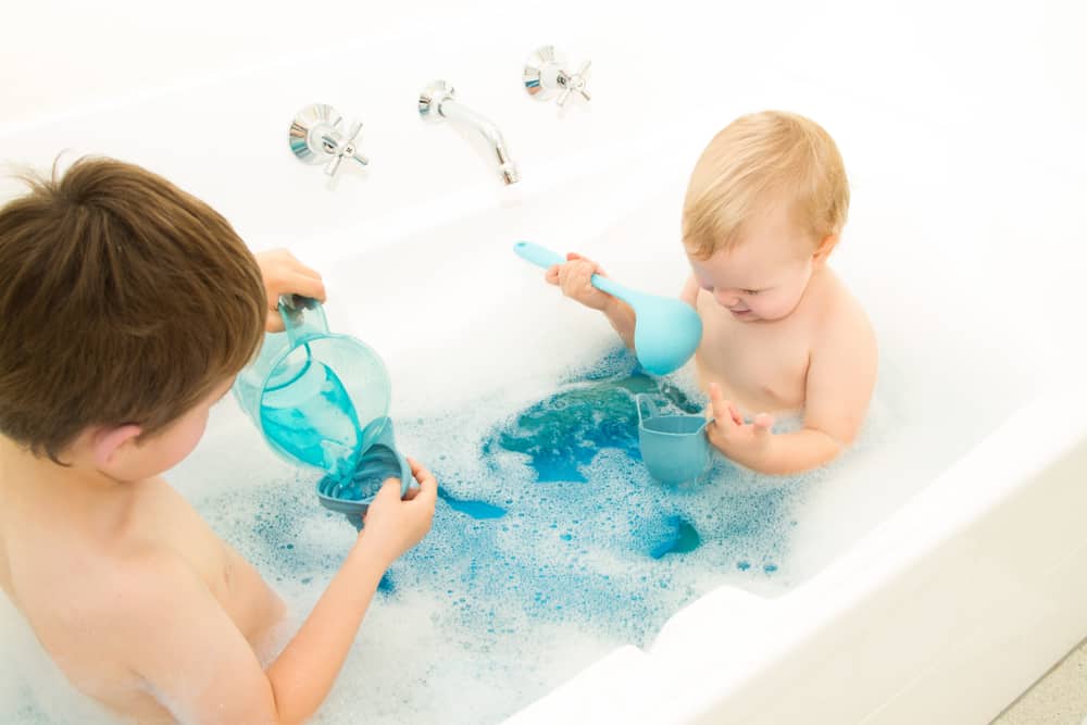 These are a couple of boys playing with cups and ladles at the bathtub.