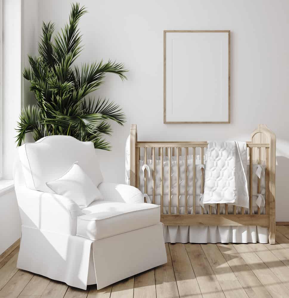 Nursery room with a skirted wooden crib and a white armchair over wide plank flooring.