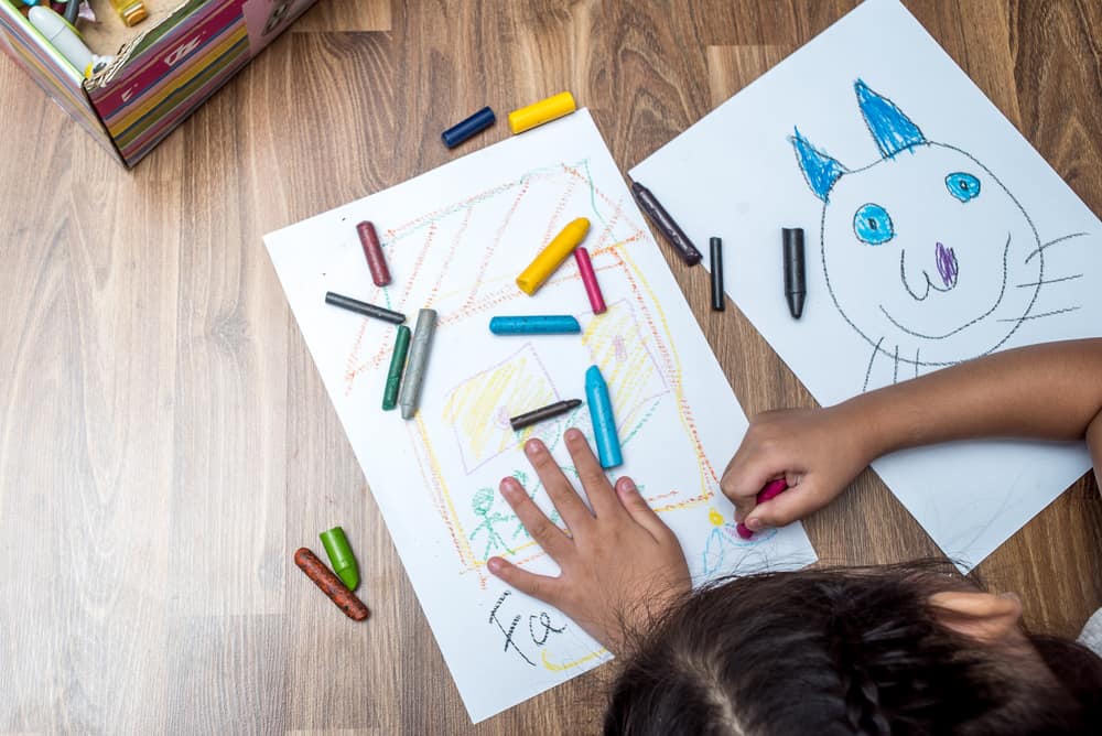 Coloring toys: A kid using crayons to color on pieces of paper. 