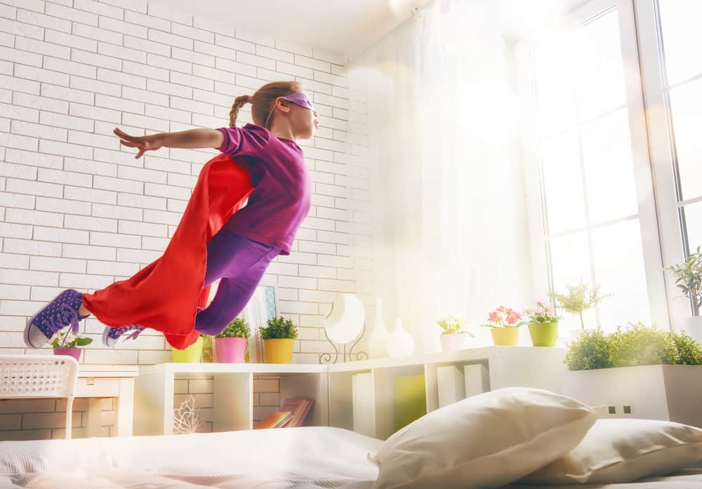 200 Best Indoor Activities for Kids 10 A kid wearing a cape playing superhero in the bedroom.