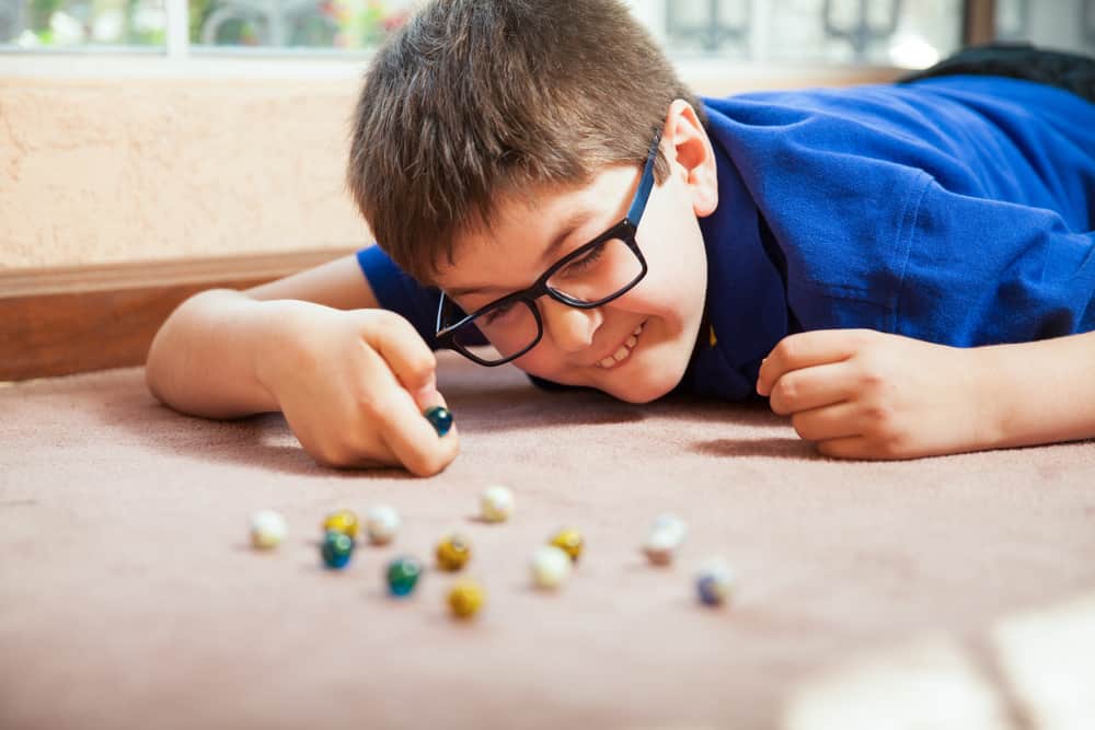 200 Best Indoor Activities for Kids 13 This is a boy playing with marbles on a carpeted floor.
