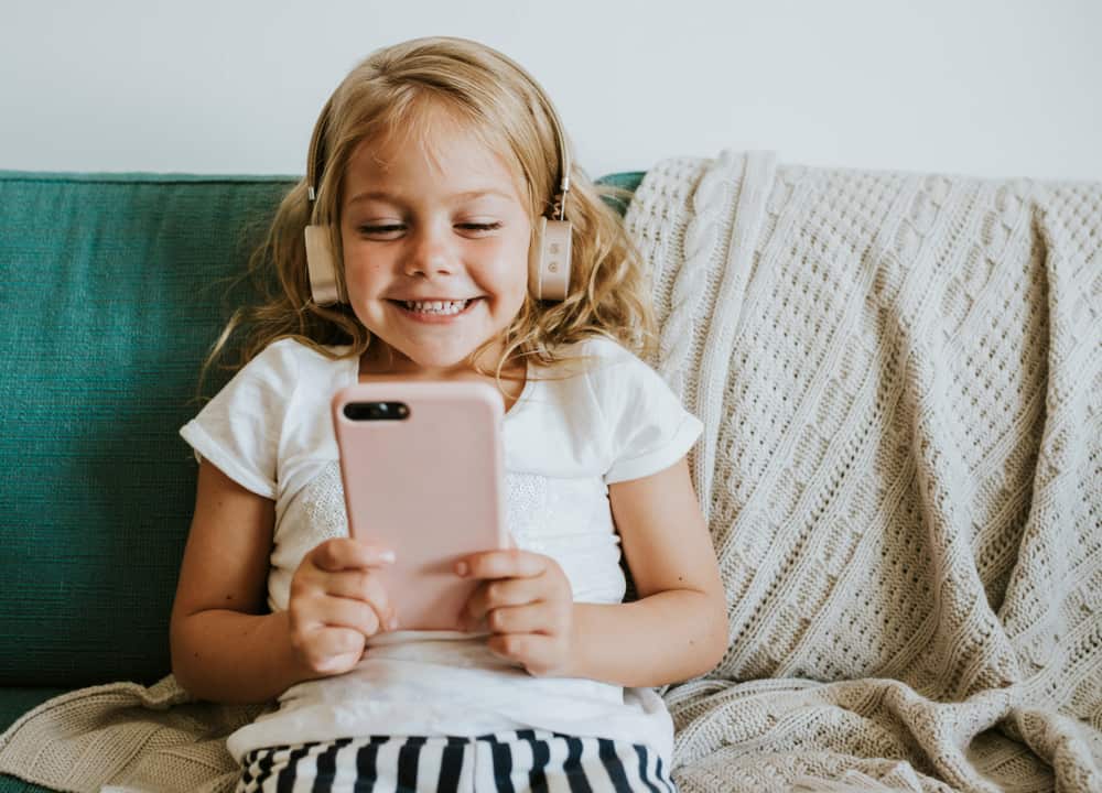 200 Best Indoor Activities for Kids 19 Indoor activities: A girl playing on a smart phone in the living room.