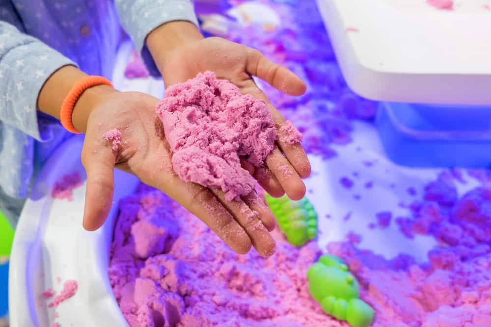 Toys similar to play dough: A close look at a kid playing with kinetic sand.