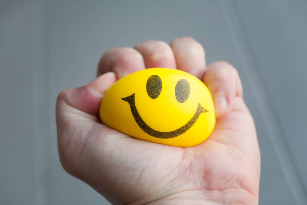 A yellow stress ball with a smiley face on it being squeezed.