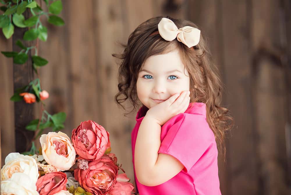 19 Best Toys for 3 Year Old Girls 1 This is a three-year-old girl wearing a bow playing with flowers.