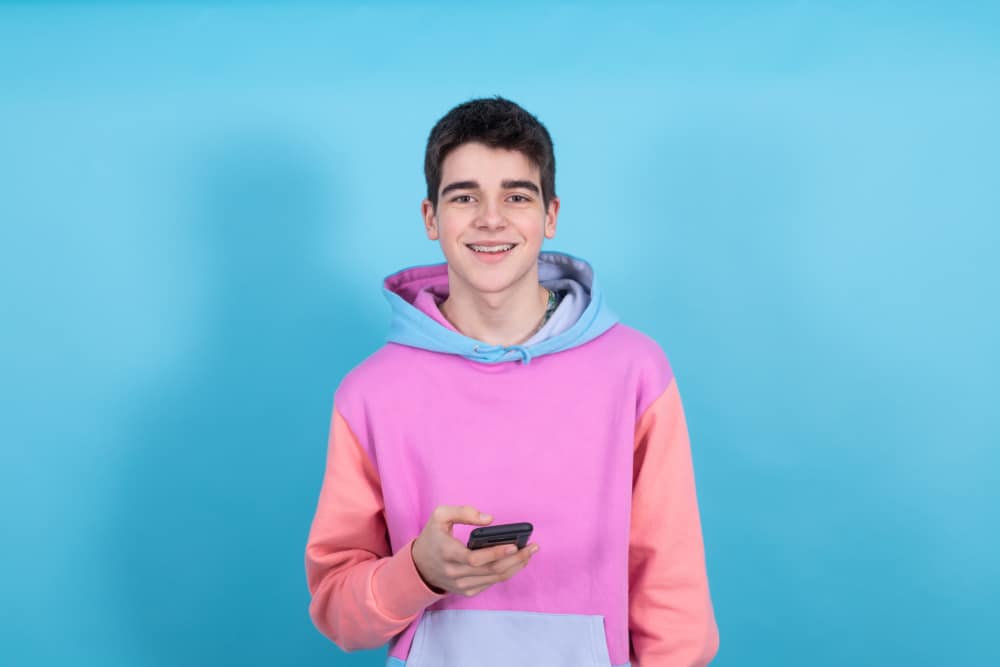 This is a thirteen-year-old boy wearing a colorful hoodie and holding his phone.