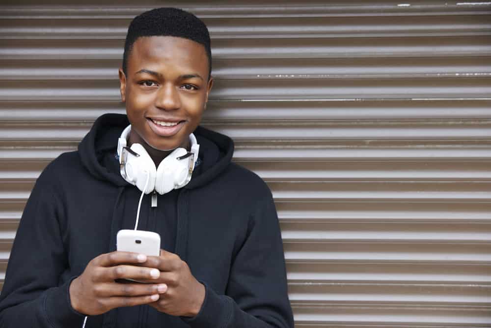 This is a 12-year-old boy wearing a black hoodie with a white headphone and smartphone.