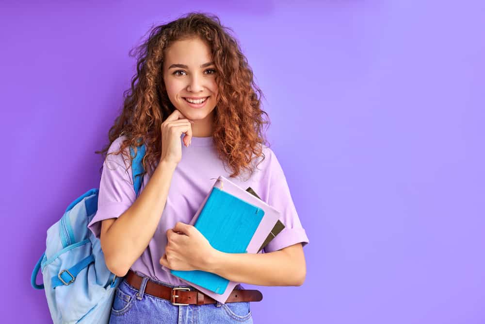 A twelve-year-old girl carrying her backpack and a stack of notebooks.