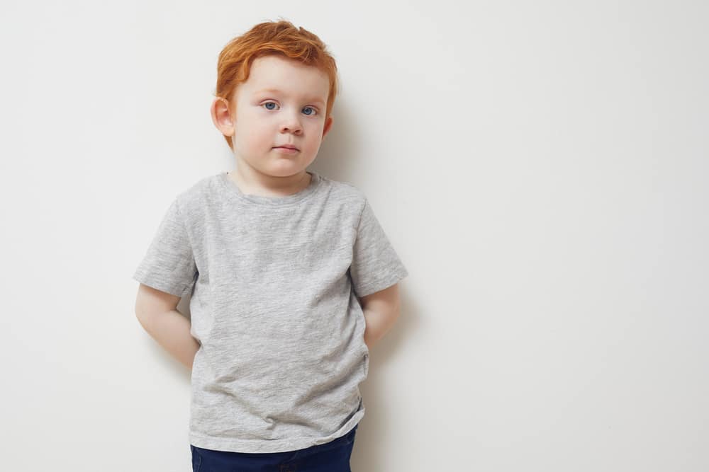 Portrait of a redhead boy standing against the white wall.