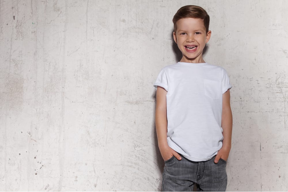 Little boy in white shirt posing against the grunge concrete wall.
