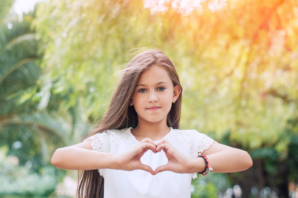 A little girl in the park with long hair creating heart shape with her hands.