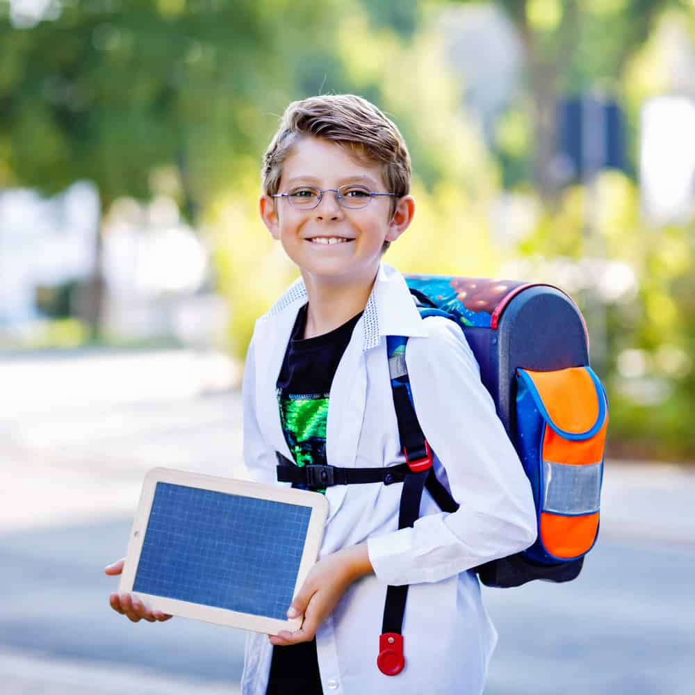 17 Best Toys for 9 Year Old Boys 1 Little boy with eyeglasses and backpack holding a chalk desk on his way to school.