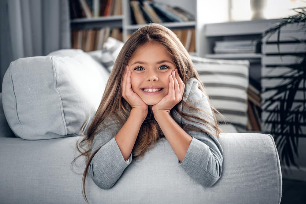 17 Best Toys for 9 Year Old Girls 1 Little girl with long, blonde hair comfortably lying on the couch.