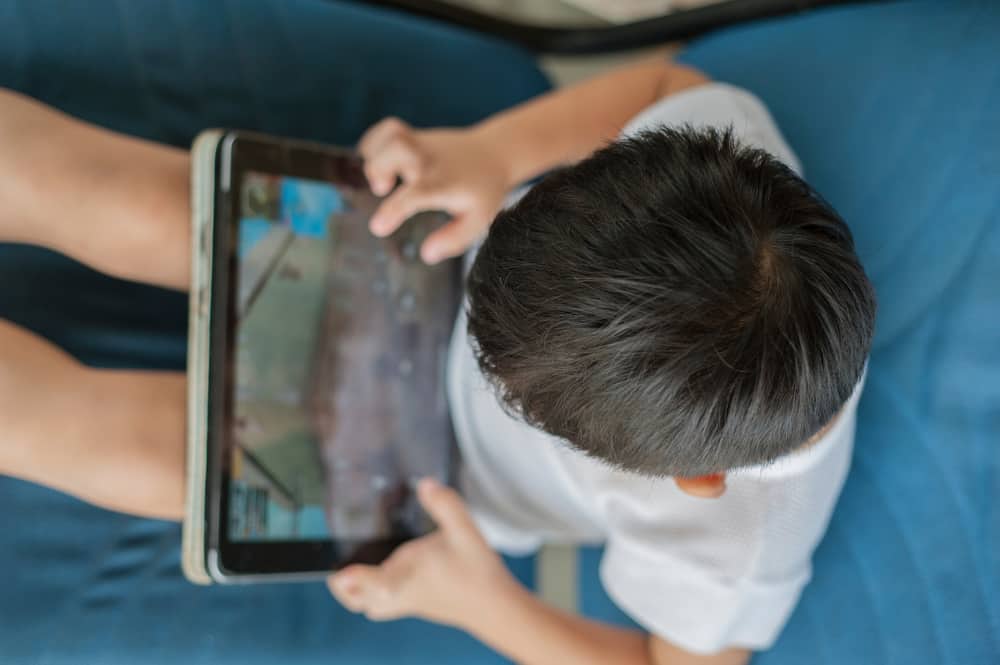 50 Best Science Activities for Kids 3 Little boy sitting on a couch playing games on a tablet.