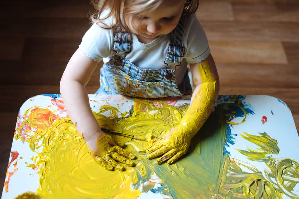 50 Best Art Activities for Kids 1 A girl painting with her hands on the table using yellow paint.
