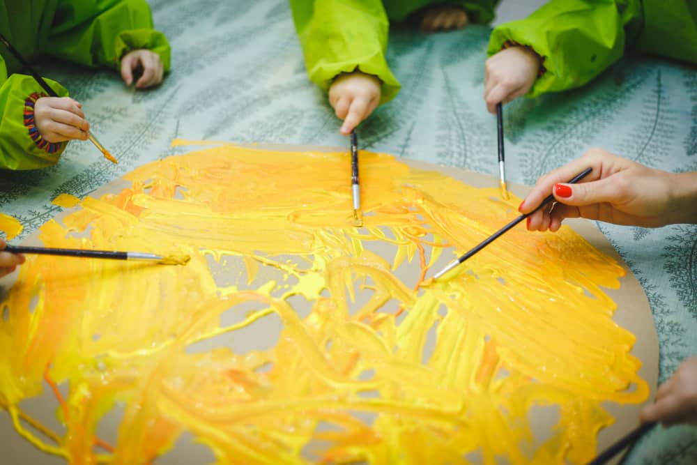Art activities for kids: Small kids with teacher doing a collaborative circle painting using paint brush.