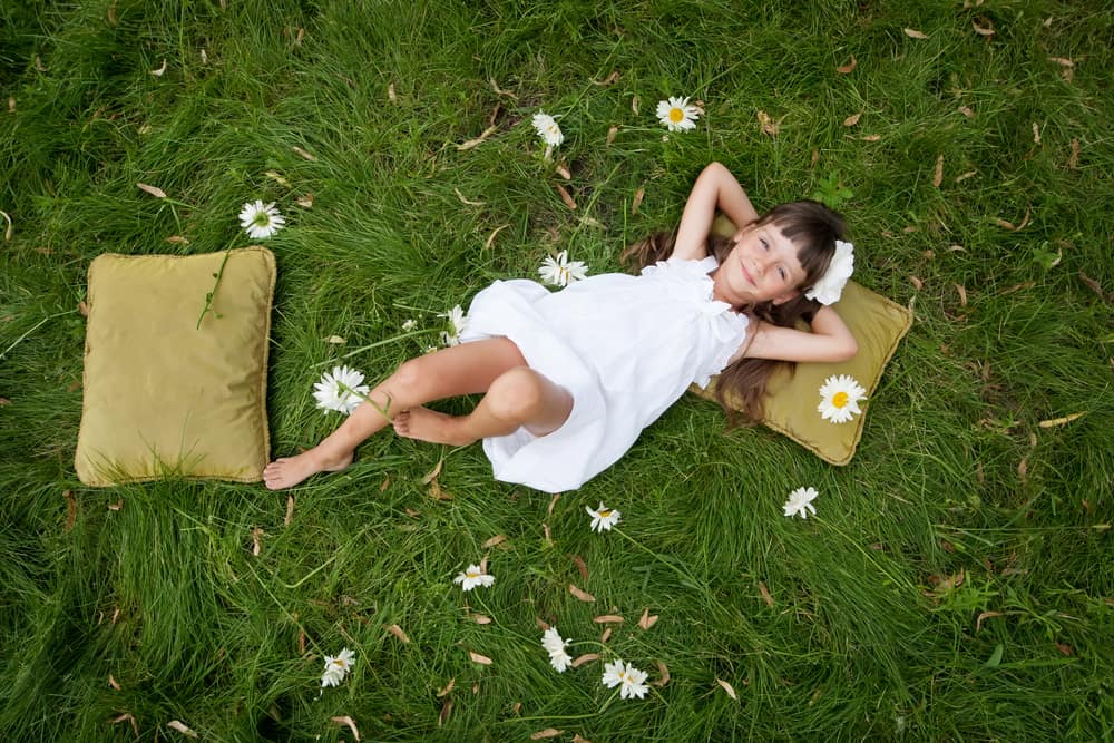 50 Best Nature Activities for Kids 1 Little girl resting on soft pillow in fresh spring grass with white daisies.