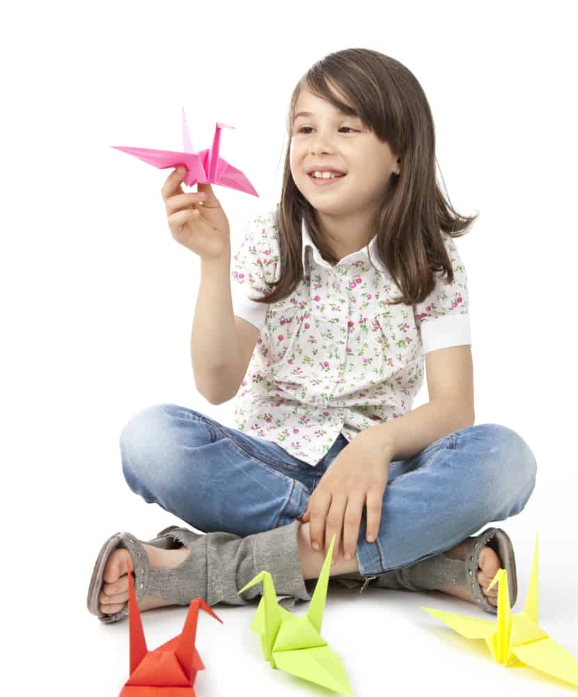 Girl on a cross sitting position holding an origami bird.