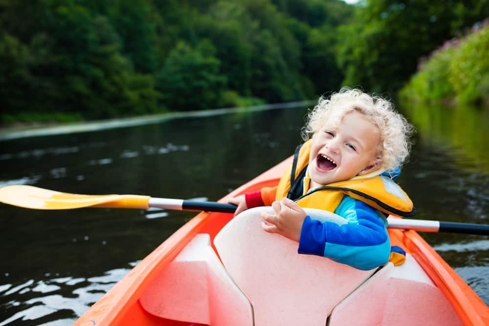Little boy kayaking on a river during a summer day.