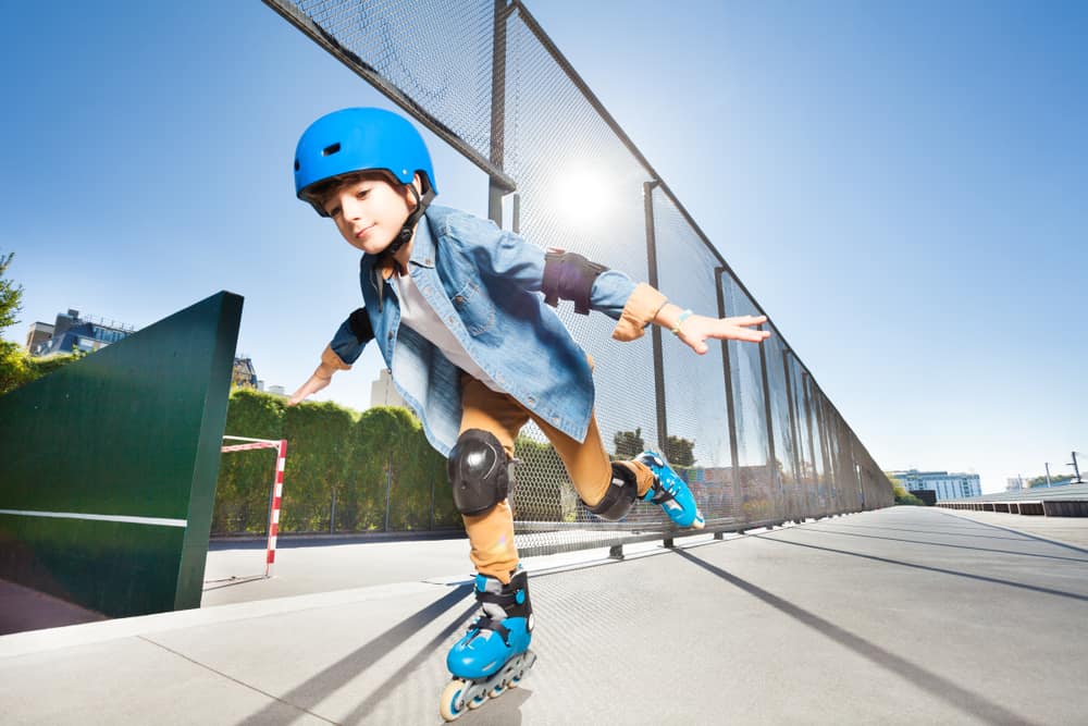 Little boy equipped with head gear and pads doing tricks at skate park.