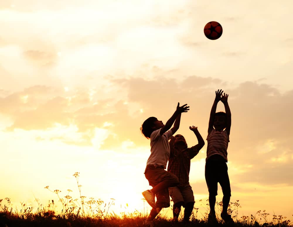 50 Best Sports Activities for Kids 1 Sports activities for kids: Group of kids playing with ball during sunset.