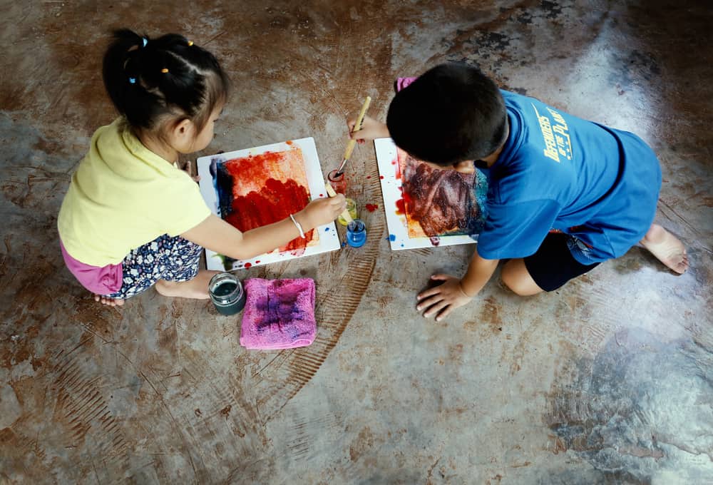 Little kids painting water colors on rustic concrete floor.