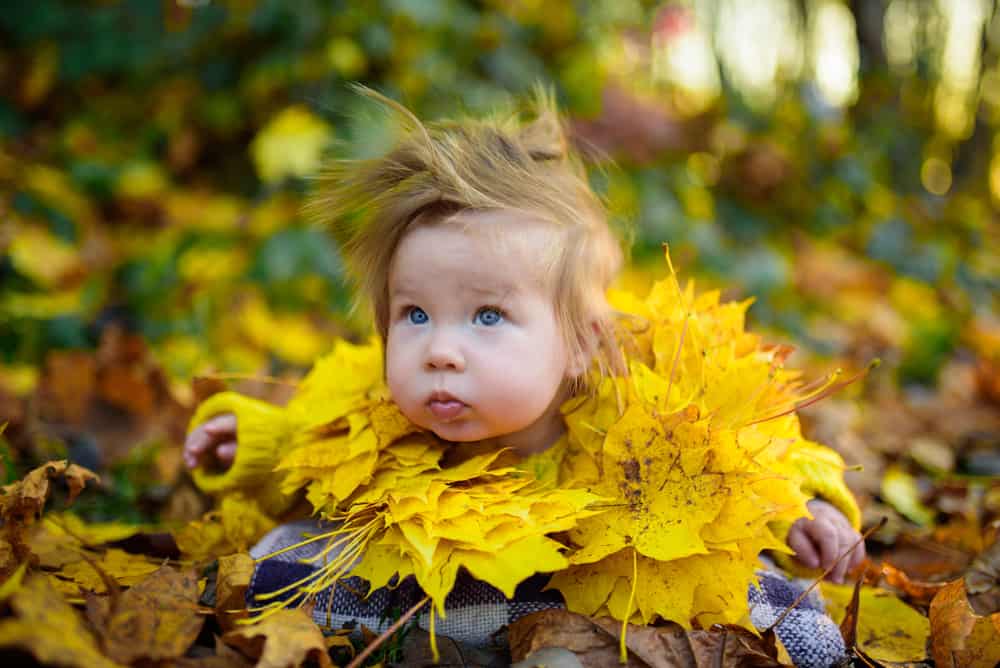 Little girl wearing autumn leaf necklace plays outdoors.