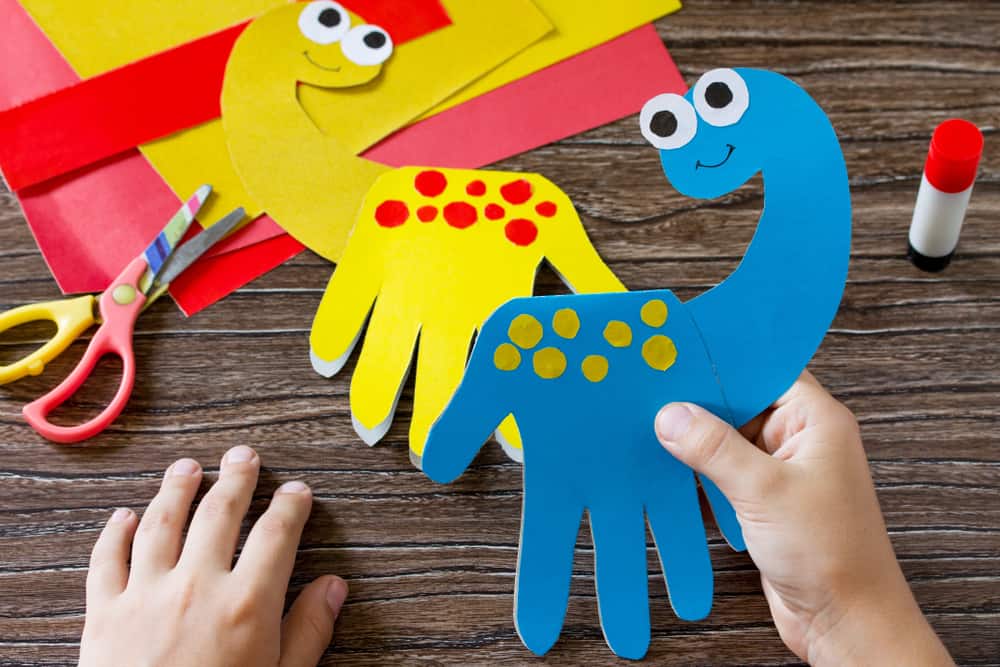 Kid holding a blue paper plate dinosaur that he created on the wooden table.