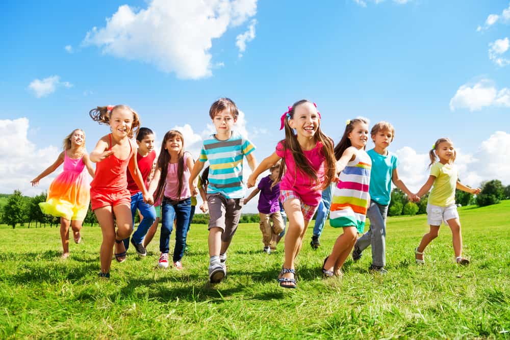 Group activities for kids: A large group of children playing on a wide grass field.