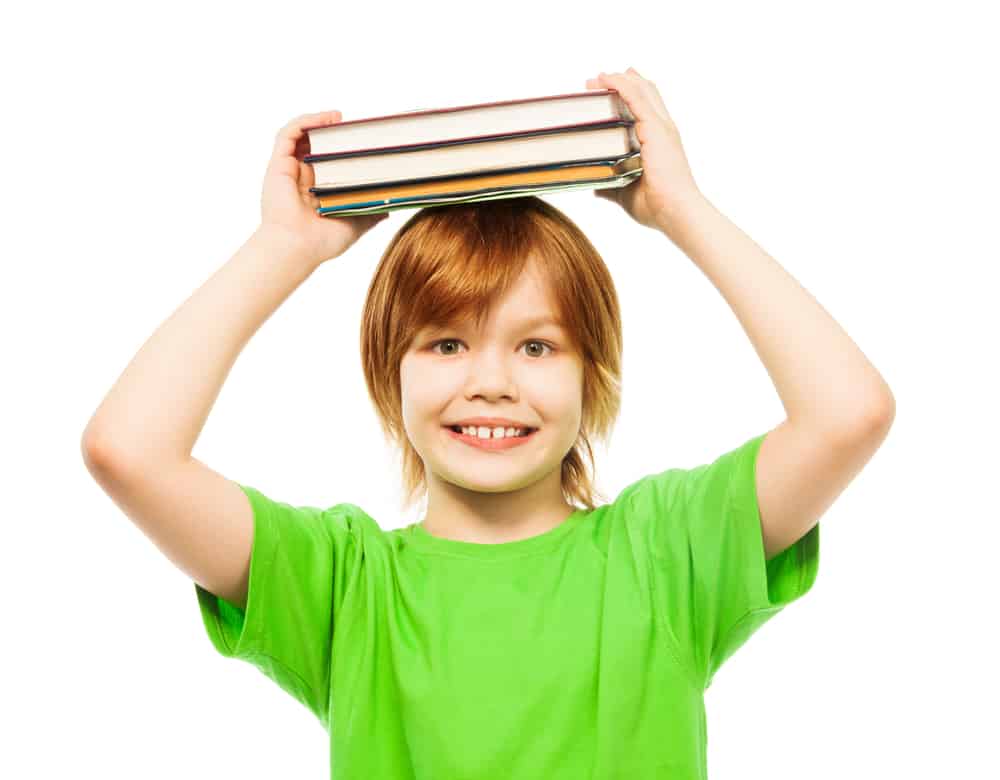 An eight-year-old boy in a green shirt carrying books over his head.