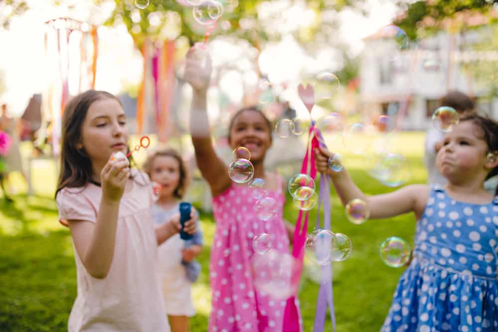 100 Best Kids Birthday Party Ideas 8 Kids playing bubbles outdoors.