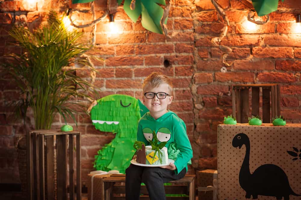 100 Best Kids Birthday Party Ideas 13 Boy in eyeglasses celebrating his birthday with a dinosaur theme.