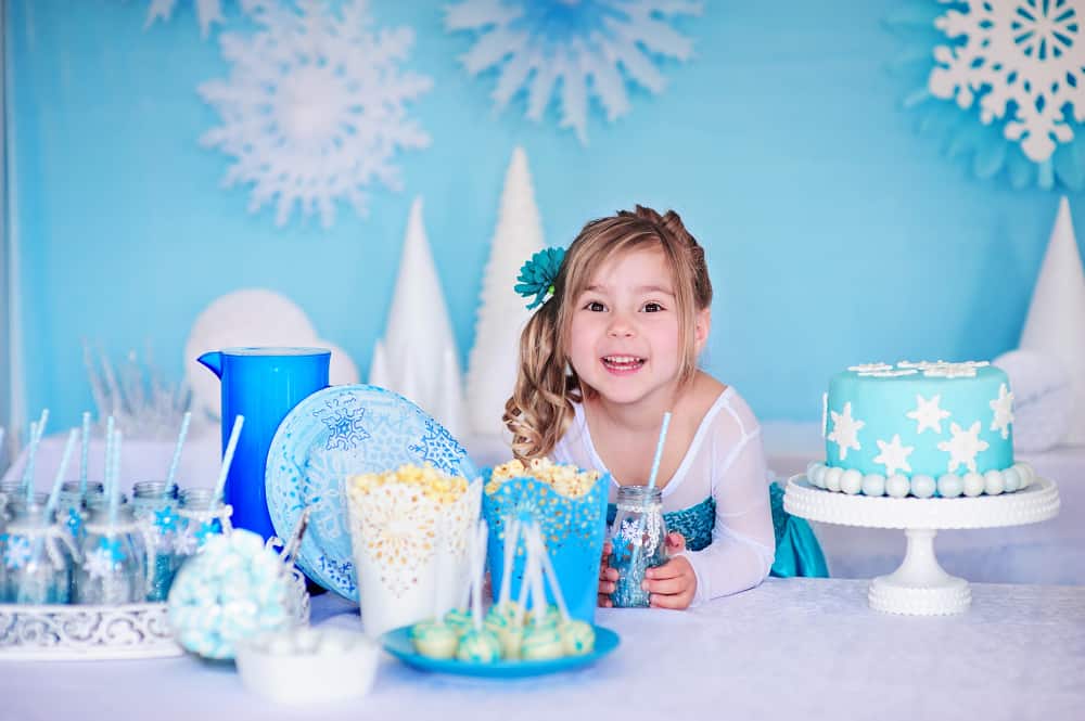 100 Best Kids Birthday Party Ideas 4 Little girl wearing Elsa costume in a Frozen-themed birthday party with snowflakes cake, popcorn, and sweets.