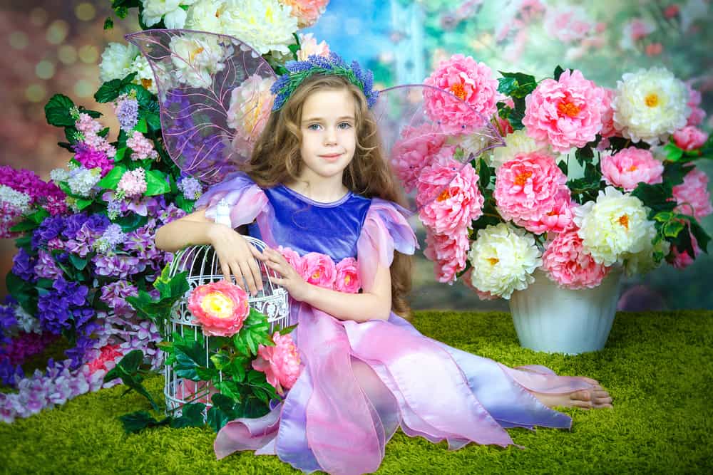100 Best Kids Birthday Party Ideas 5 Little girl wearing a fairy costume is surrounded by decorative flowers.